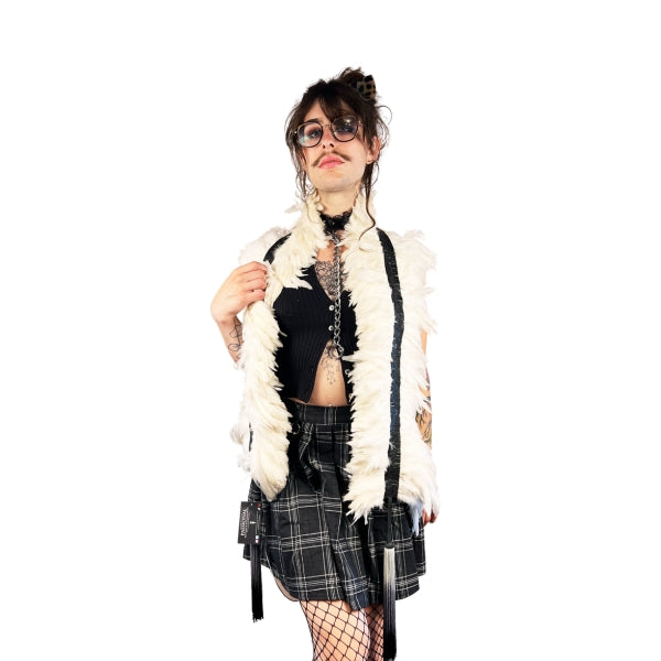 A model in a pleated skirt, black top and fishnets, wearing white latex feather boa draped around their shoulders.