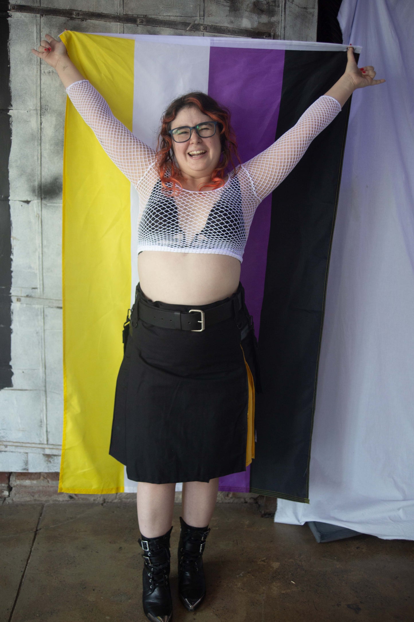 model holding Nonbinary Outdoor flag behind them, while wearing the Nonbinary Pride Flag Heritage Kilt