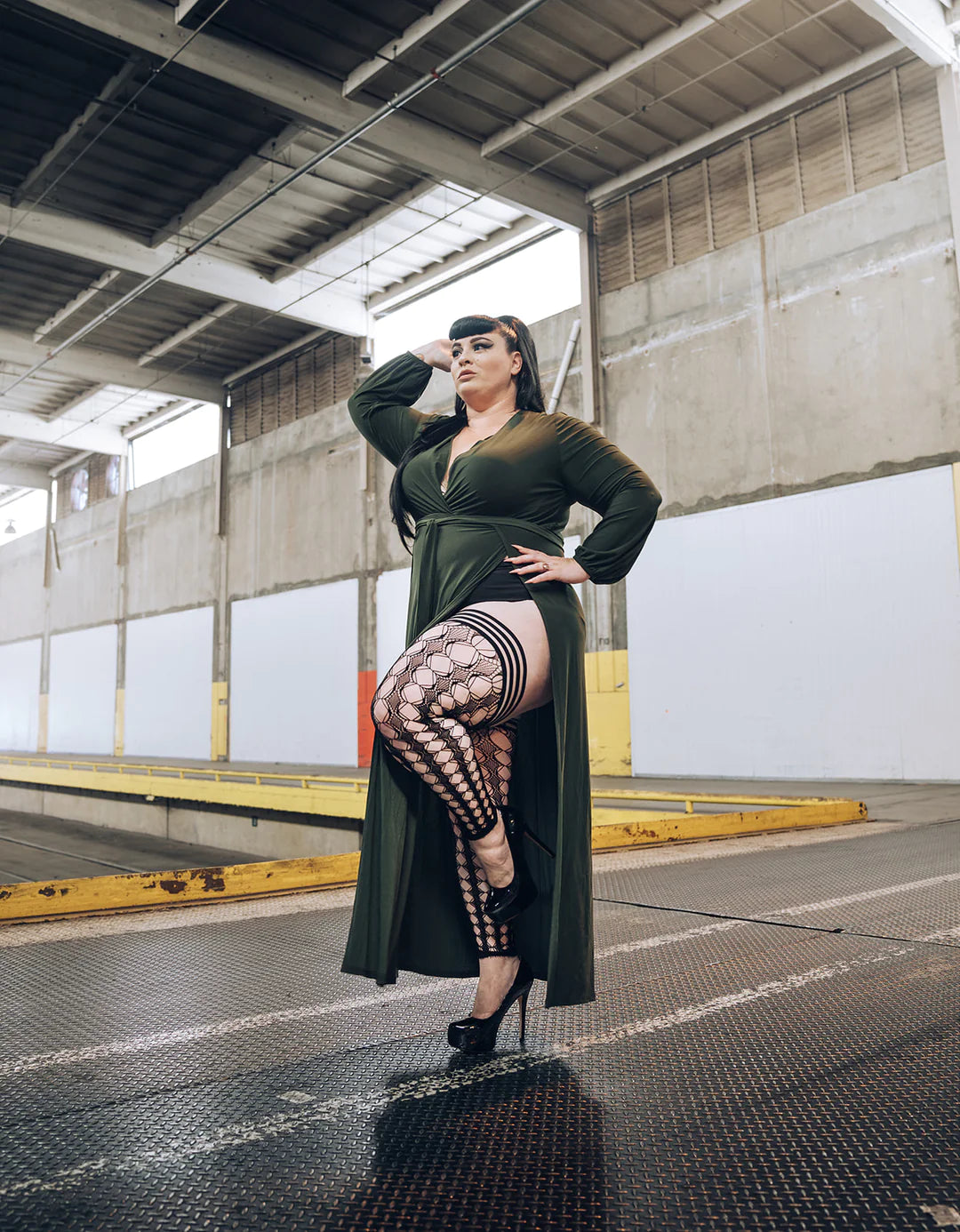 Model on train platform wearing black dress with slip , left leg raised wearing Jo Footless Thigh Highs