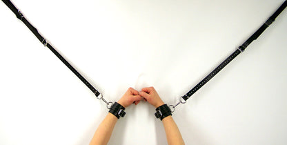 2 black leather bed tie downs connected to cuffs on a model's wrist.