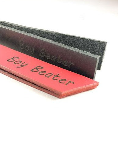 A red and a black 1 inch leather slapper with the words boy beater printed on the body.