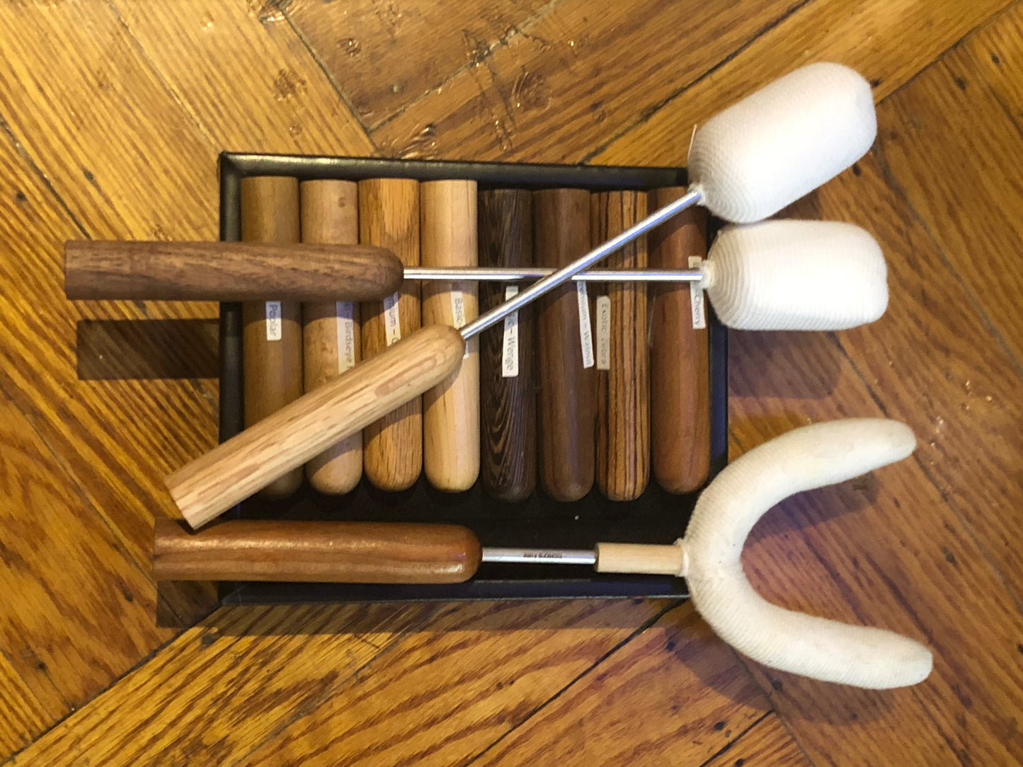 A box with several wood handles displayed inside. Three different fire torches lay on top of the handles.