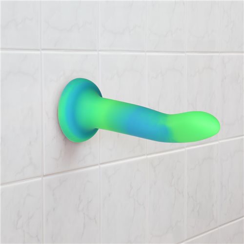 The blue and green Rave Addiction 8" Glow in the Dark Dildo suctioned to a wall.