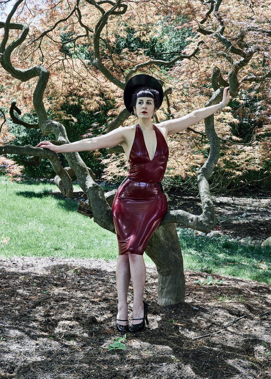 Model sitting outside on a low tree limb showing the front of the Black and Plum Curvy Pencil Panel Skirt.