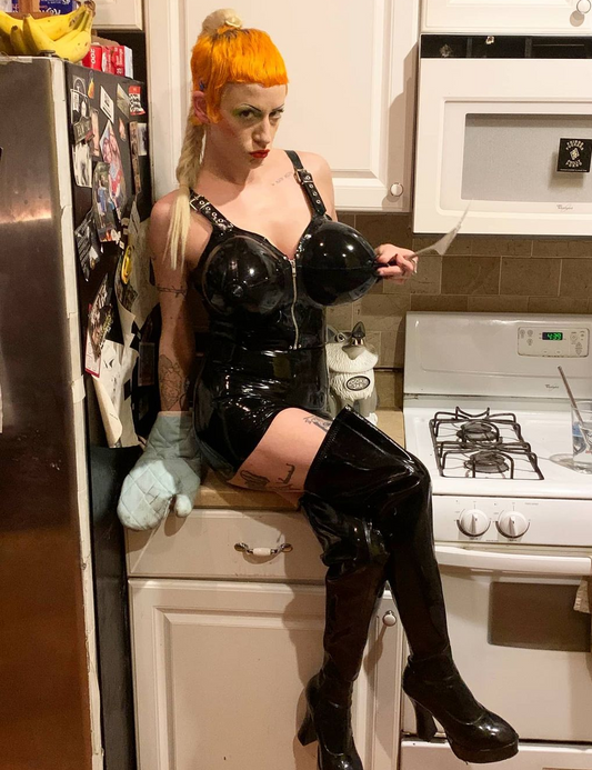 A model wearing the DeMask Inflatable Torpedo Tatas Top with a matching skirt and thigh high boots.