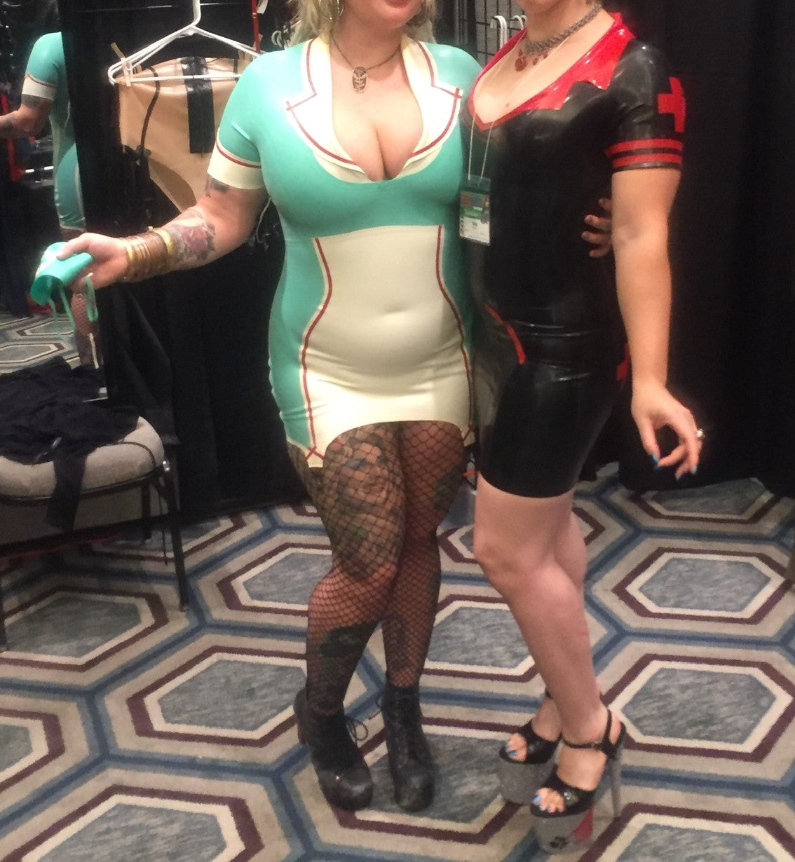 Two models wearing latex nurse costumes. One is black and red and the other is the Latex Natasha Nurse Dress & Cap.