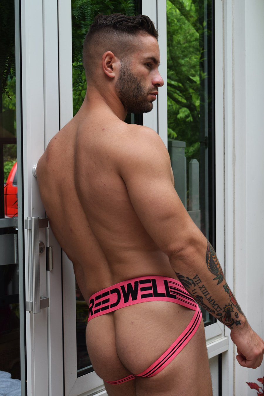 Model wearing neon pink CumDump Jockstrap, rear view.