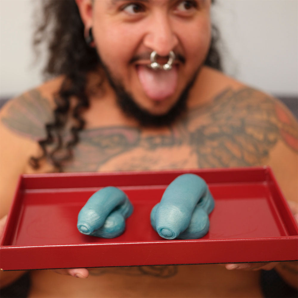 A model holding up a red tray with two different sized teal Pierre Packer Penises.