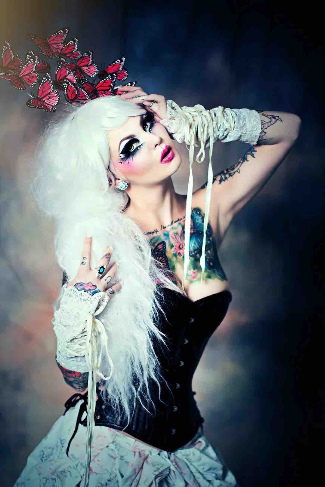 A model with long white hair and white lace gloves wearing the Black Leather Short Overbust Corset -Slim over a floral skirt.