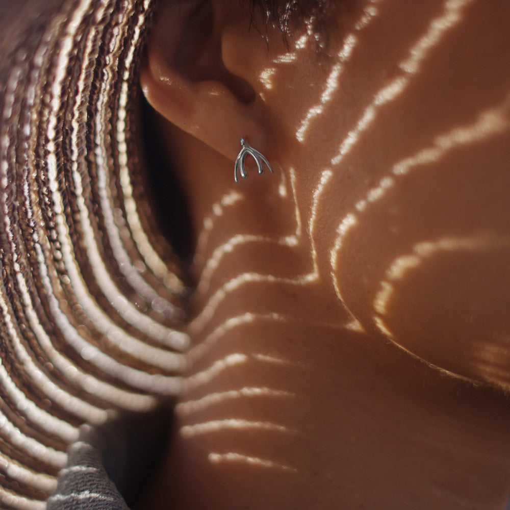 A close up of the Clit Earrings on a model wearing a sun hat. The sun shining through reflects stripes on the side of the model's face.