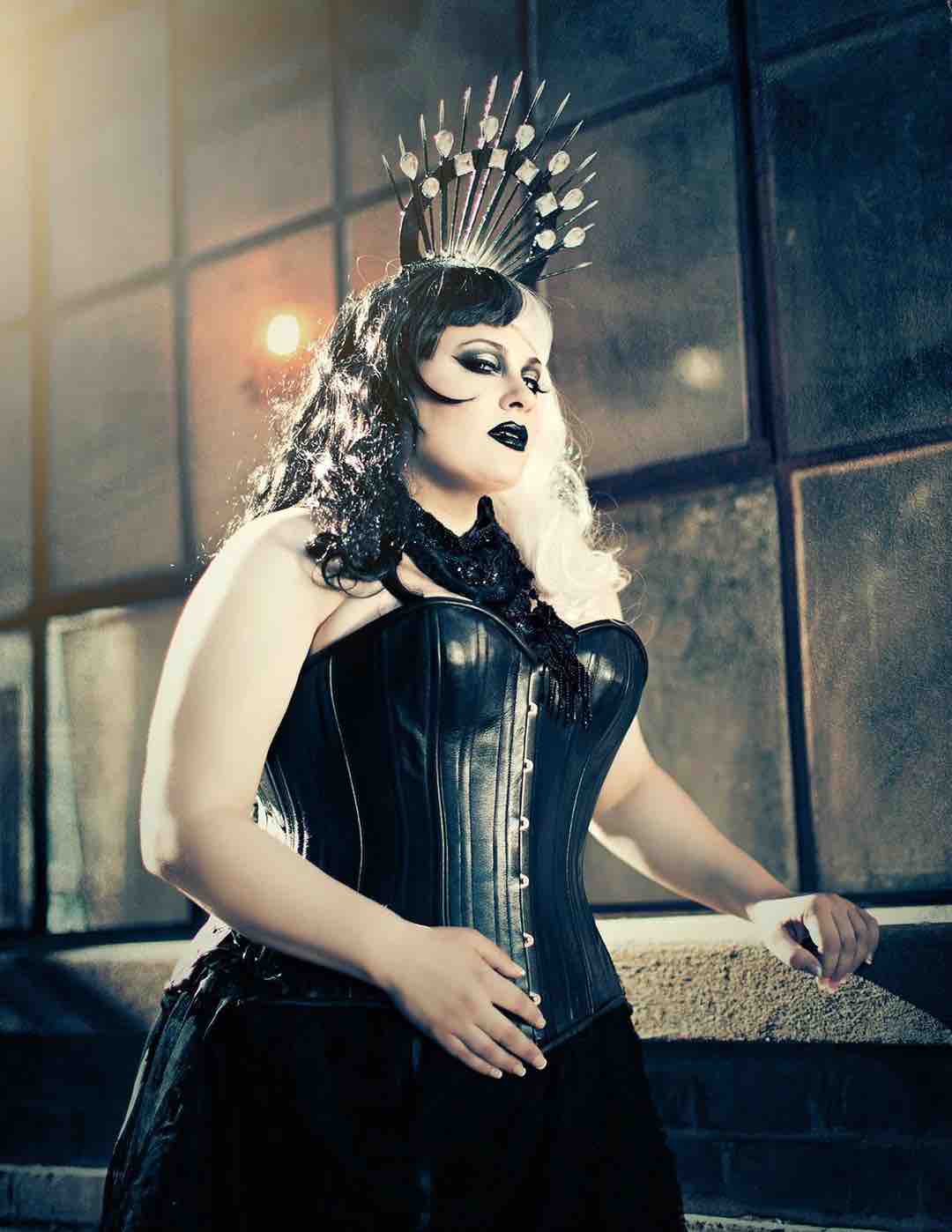 A plus size model with a spiked headdress wearing the Black Leather Short Overbust Corset -Slim over a black skirt.