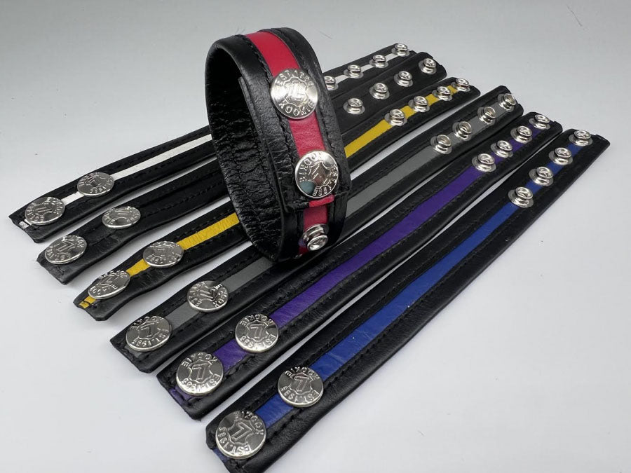 A black and red closed cock ring atop six other colorful Stripe Leather Cock Rings lying flat.