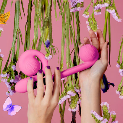 A model's hands holding the pink Snail Vibe in front of a background of flowers and butterflies.