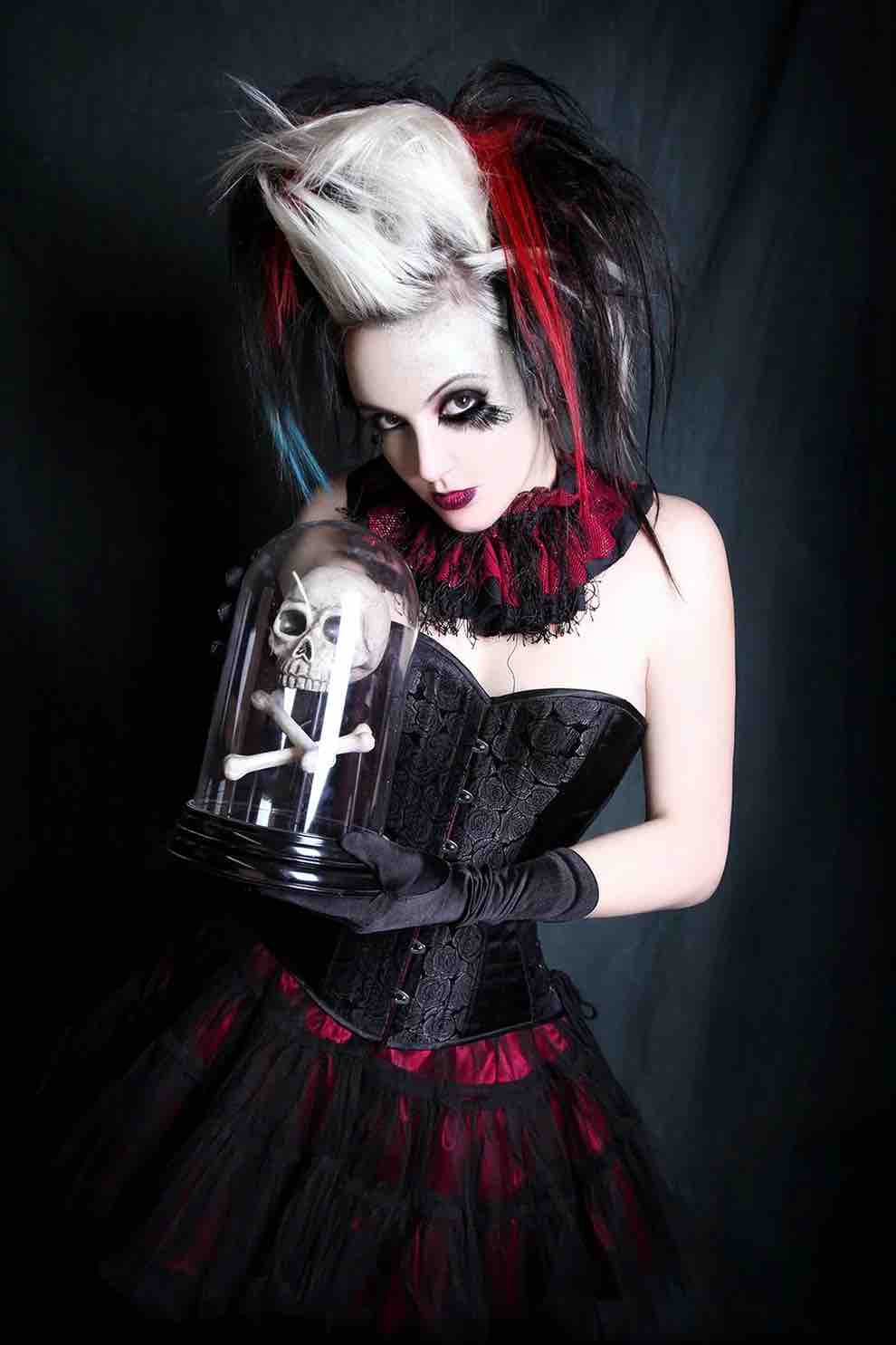A goth looking model wears the Black Rose Brocade Short Overbust Corset in Slim Silhouette over a red and black skirt.