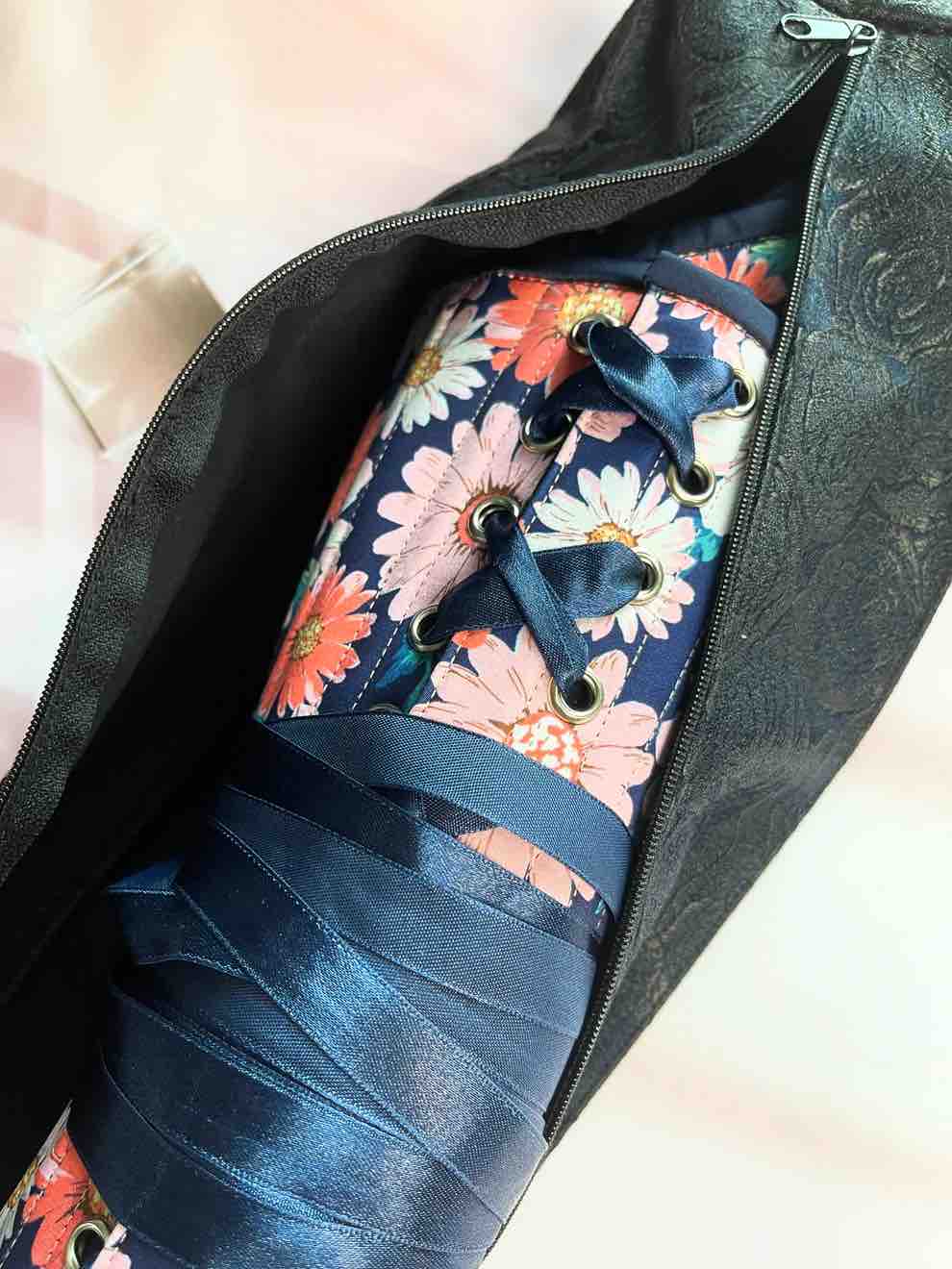 A corset with a flower pattern being placed into the black brocade Underbust Corset Bag.