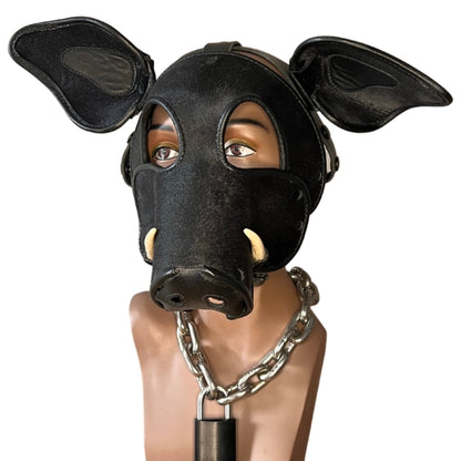 The front of the black long short snout boar mask with tusks on a mannequin head wearing a heavy metal chain with lock around its neck.