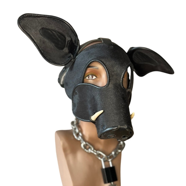 The front and right side of the black long short snout boar mask with tusks on a mannequin head wearing a heavy metal chain with lock around its neck.