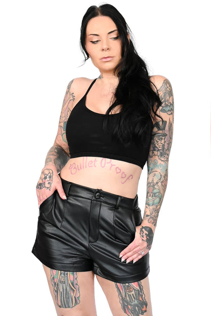 A heavily tattooed model wearing a black halter top with the Faux Leather Shorts, front view.