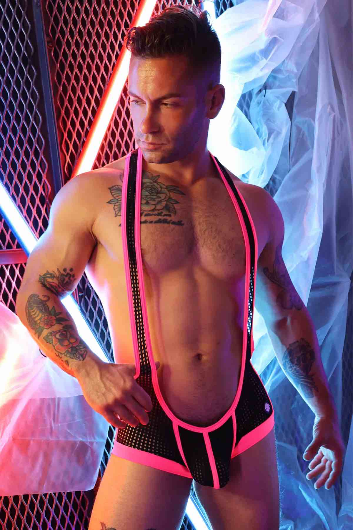 A model wearing the pink and black Dirty Boy Neon Trim Singlet against a fence lit with neon lights, front view.