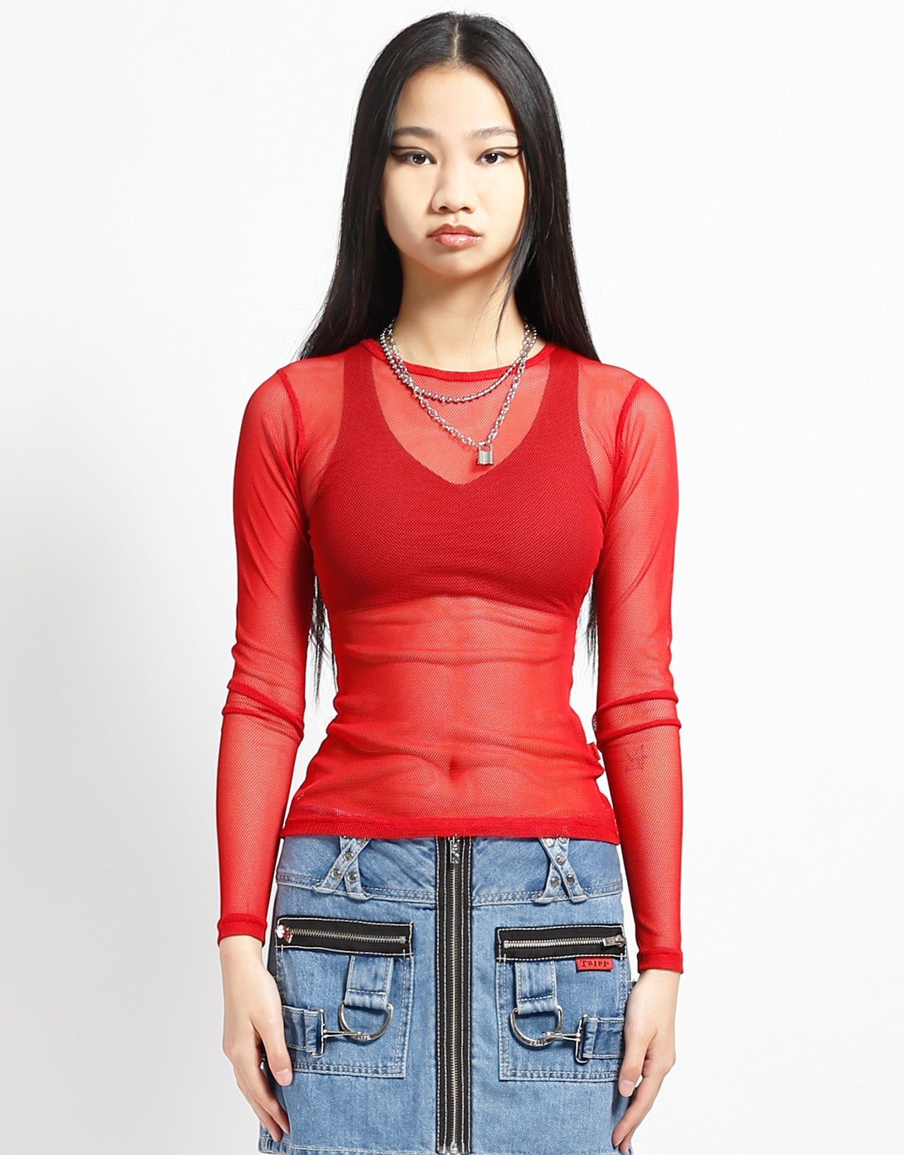 A model wearing the red Long Sleeve Baby Doll Fishnet Shirt with black bra and blue jean skirt, front view.