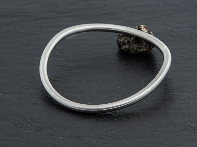 The Brushed Steel Talena Collar displayed leaning against a small rock.