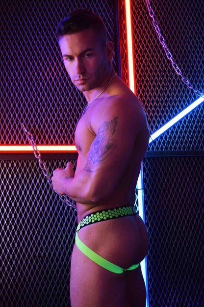 A model in front of a fence with neon lighting wears the neon green Hex Jock, side view.