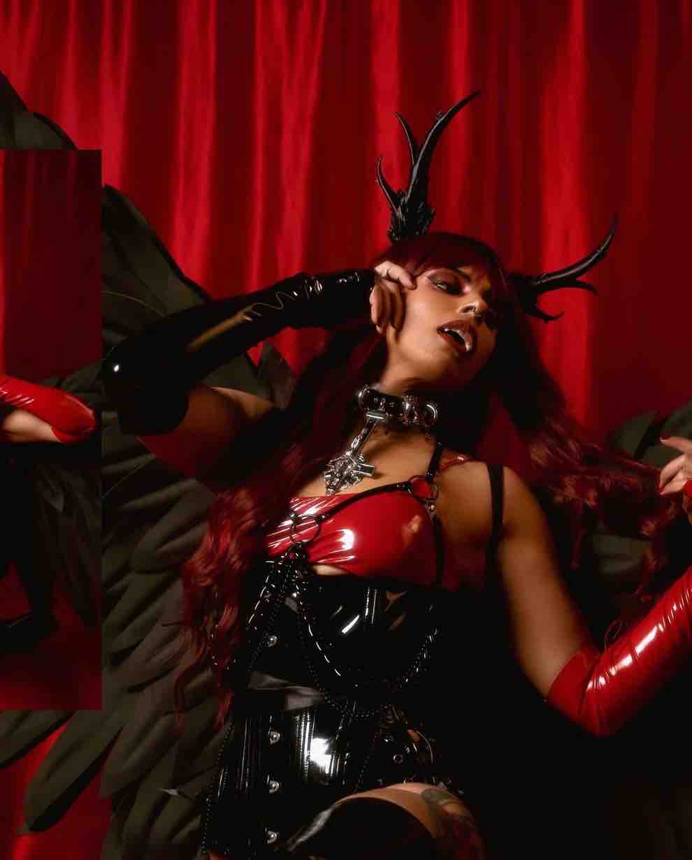 A cosplayer with large black wings and horns wears the Black Patent PVC Longline Underbust Corset - Hourglass over a red pvc dress.