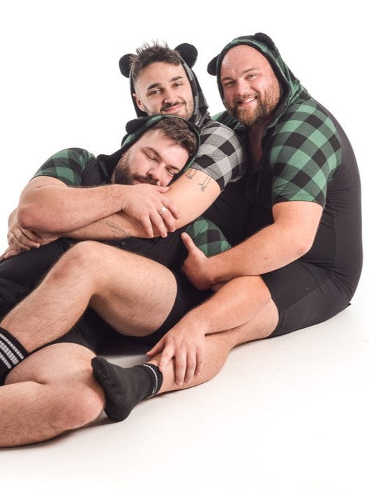 Three models wearing Plaid bamboo bear onesies in green and black as well as gray and black.