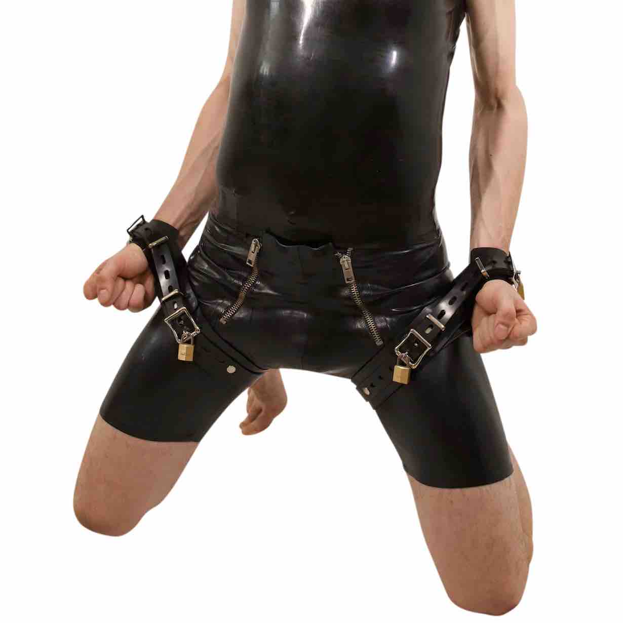 A model kneeling, wearing the Heavy Rubber Wrist to Thigh Restraint Cuffs over a black rubber outfit.