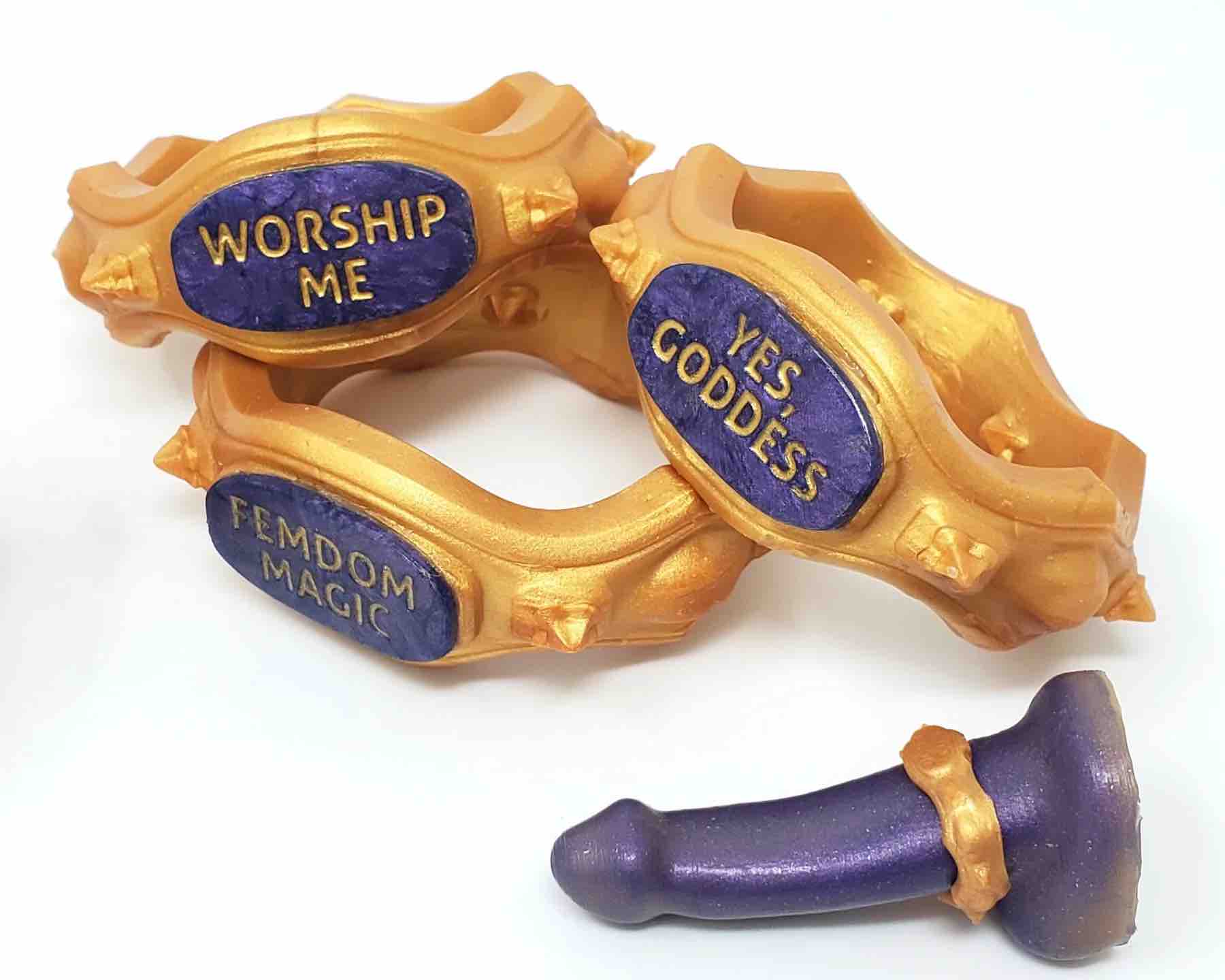 Three Royal Fetish FEMDOM Edging Body Bands with different messages along with a purple dildo with a body band on it.