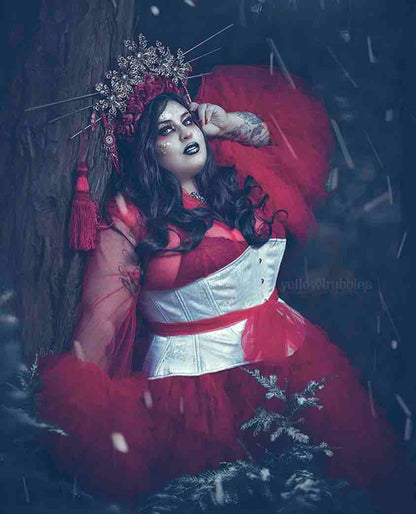 A plus size model in a silver headress wearing the White Satin Hourglass Cincher over a sheer red crinoline dress. 