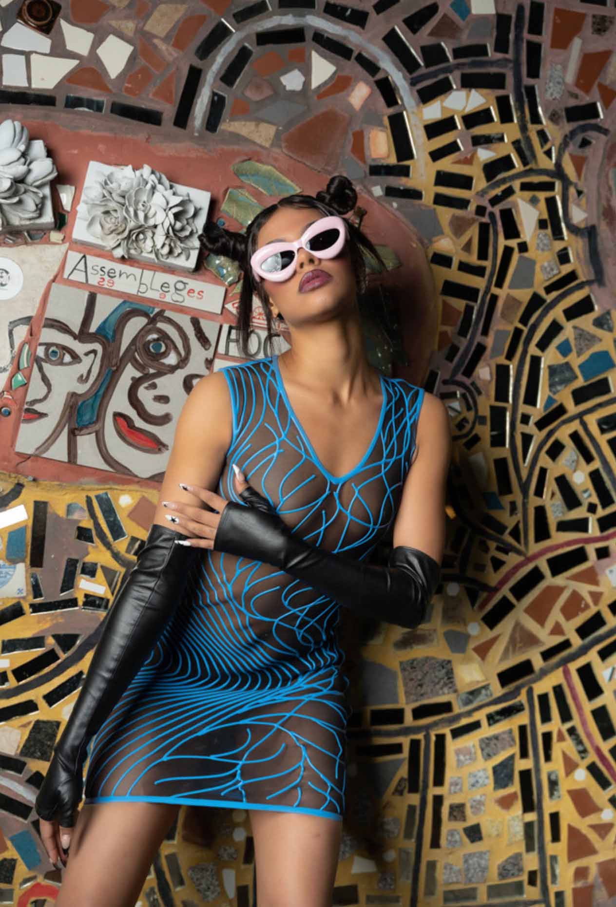 Model against mosaic wall wearing datex mesh dress with swirl pattern and elbow length black gloves