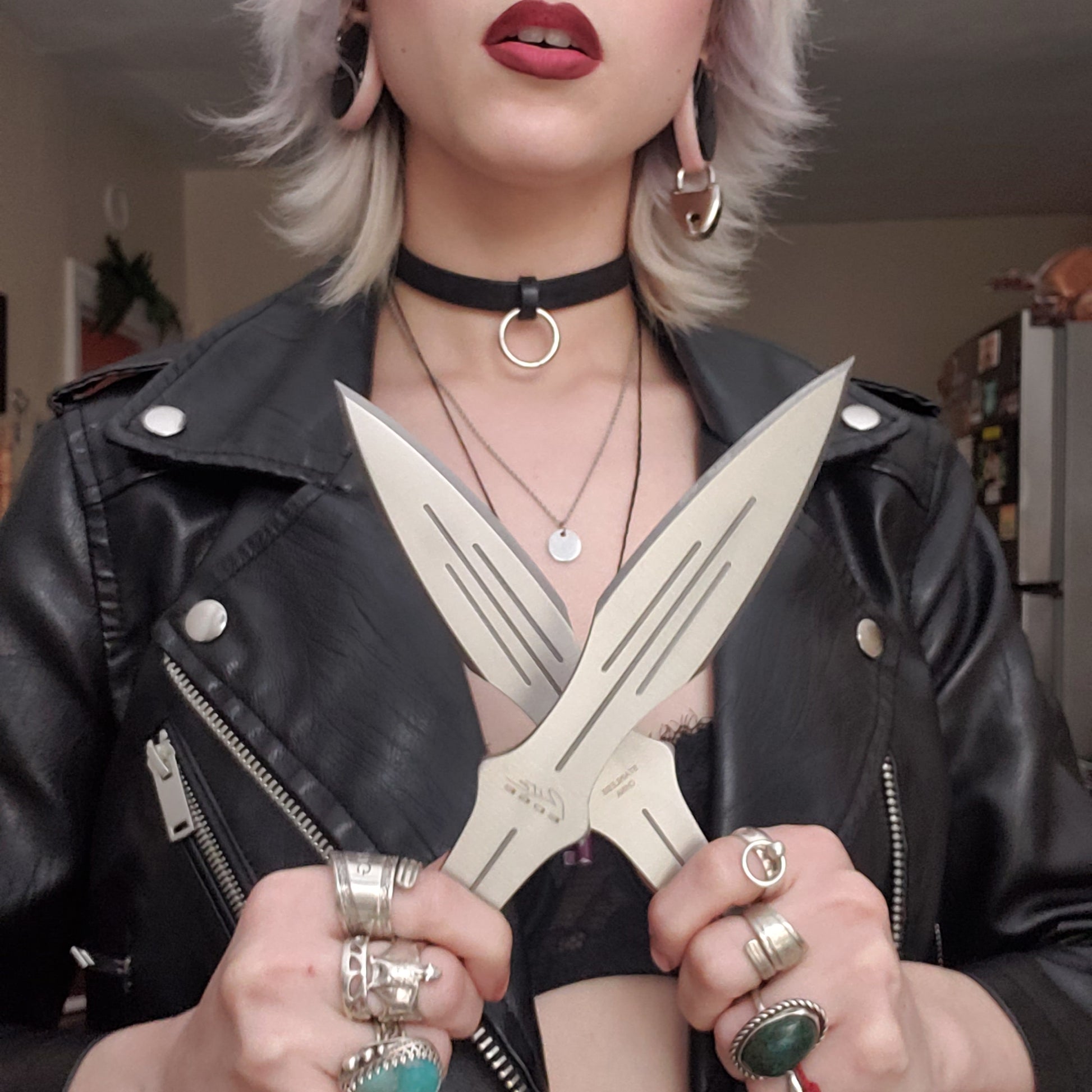 A model wearing a leather jacket holding up  two of the silver colored knives from the Pro Quality 3 Piece Throwing Knife Set.