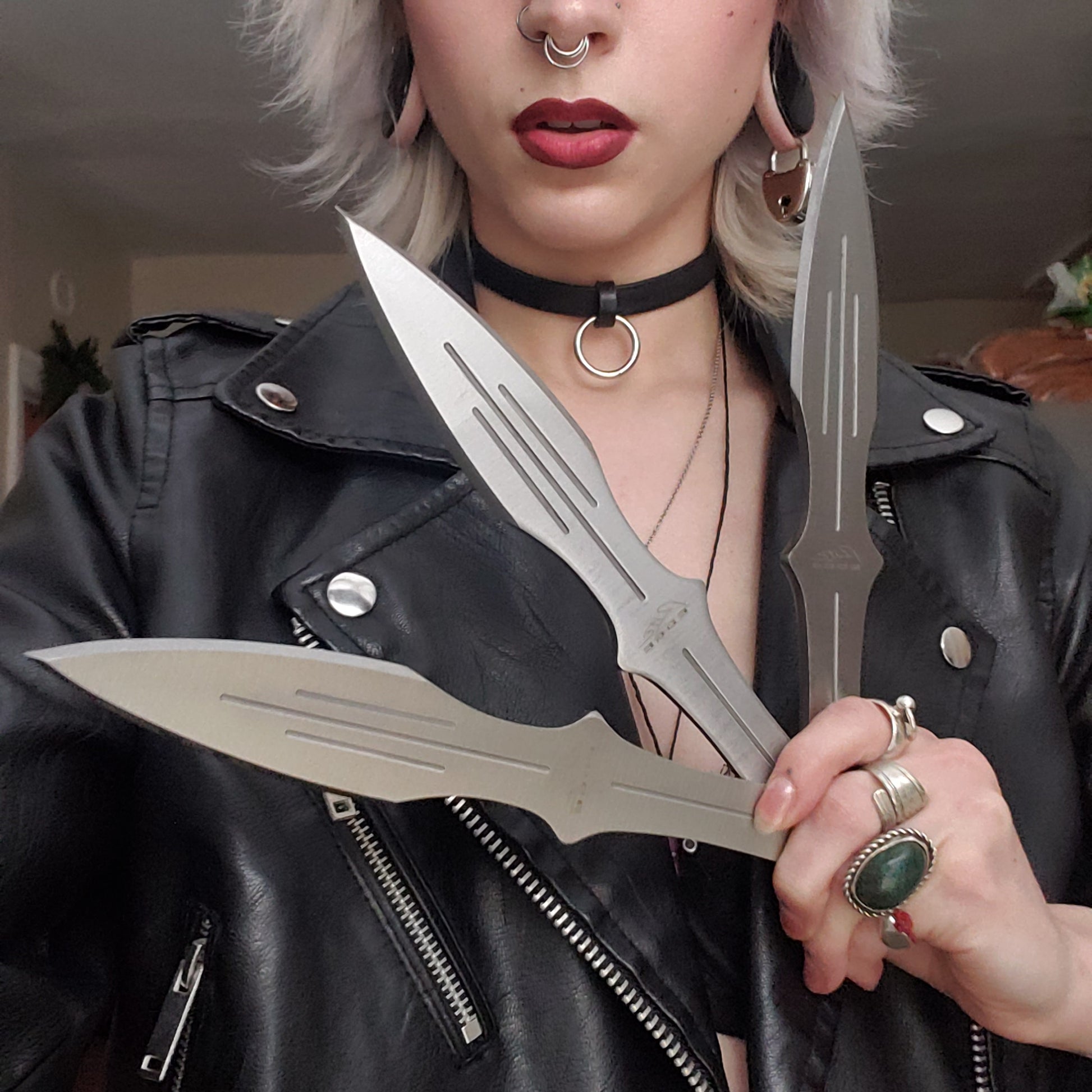 A model wearing a leather jacket holding up the silver colored Pro Quality 3 Piece Throwing Knife Set.