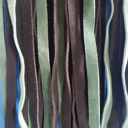 A closeup of the green and black suede finger loop flogger.
