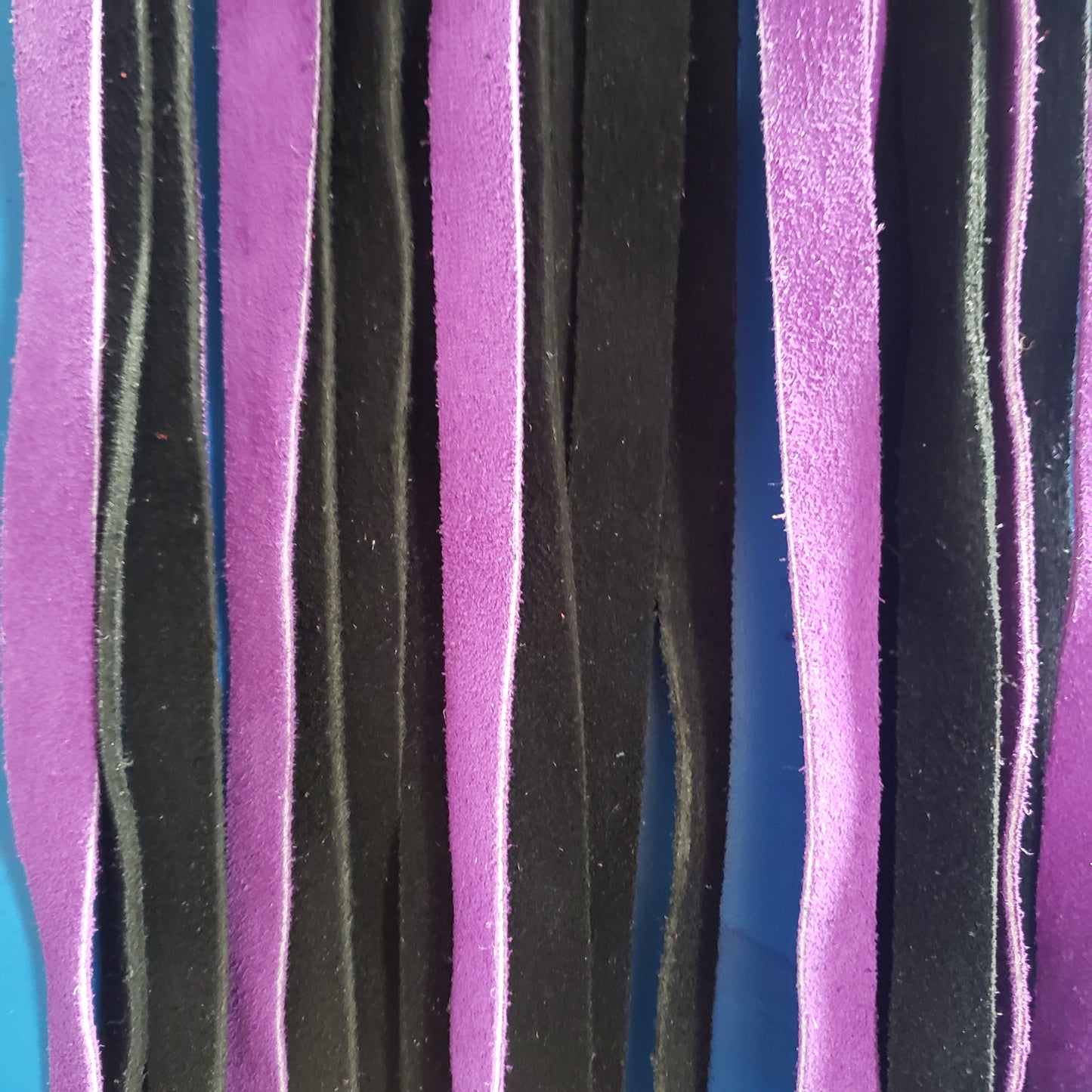 A closeup of the purple and black suede finger loop flogger.