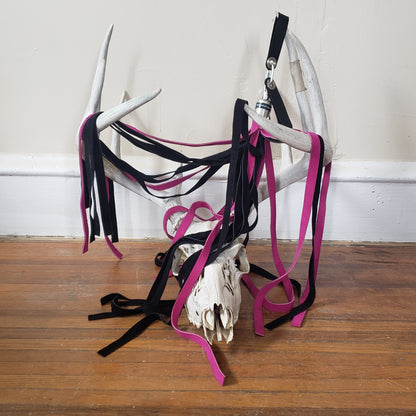 The fuchsia and black suede finger loop flogger displayed on the antlers of a deer skull.