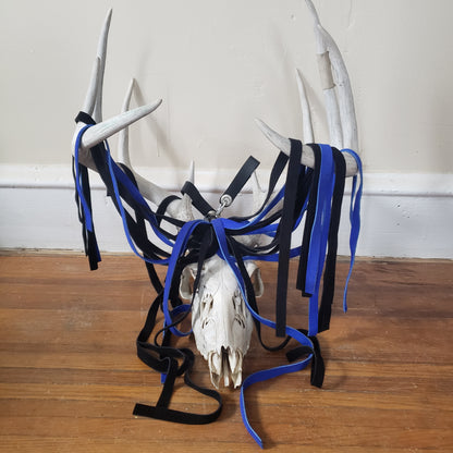 The blue and black suede finger loop flogger displayed on the antlers of a deer skull.