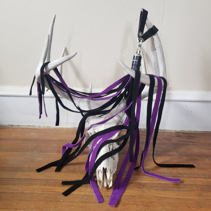 The purple and black suede finger loop flogger displayed on the antlers of a deer skull.