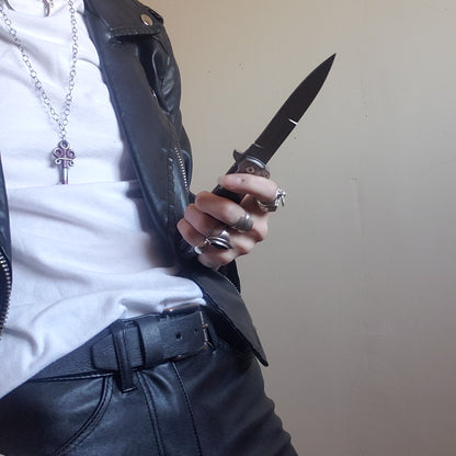 A model in a leather jacket and white t-shirt holding an open black Stiletto Type Folding Knife.