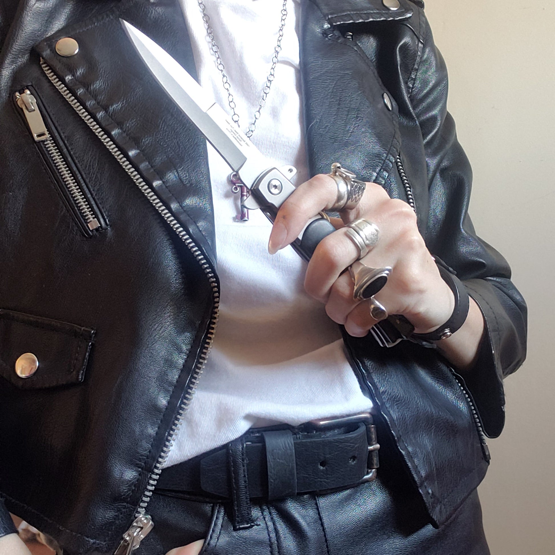 A model in a leather jacket and white t-shirt holding an open black Stiletto Type Folding Knife.
