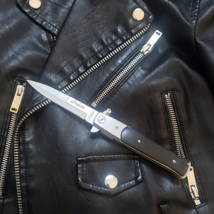 An unfolded black Stiletto Type Folding Knife laying on a leather jacket.