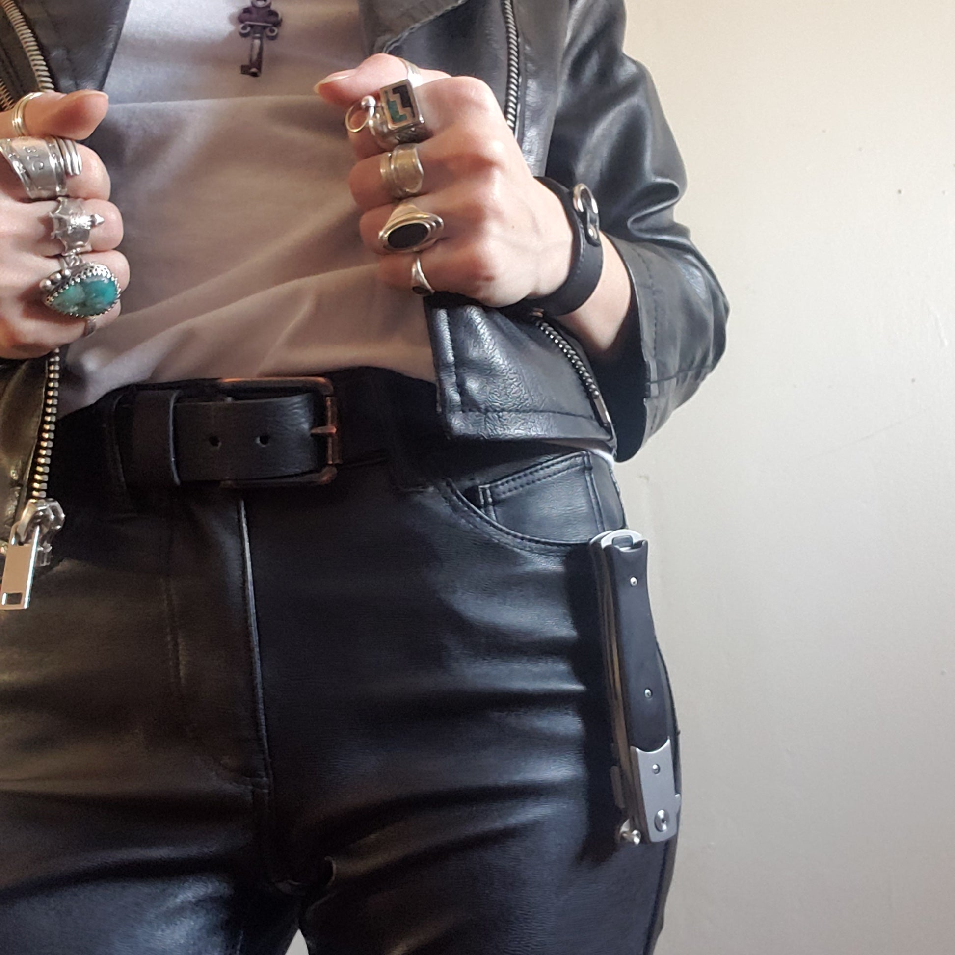 A model in a leather jacket and white t-shirt wearing a closed black Stiletto Type Folding Knife clipped onto their front pocket.