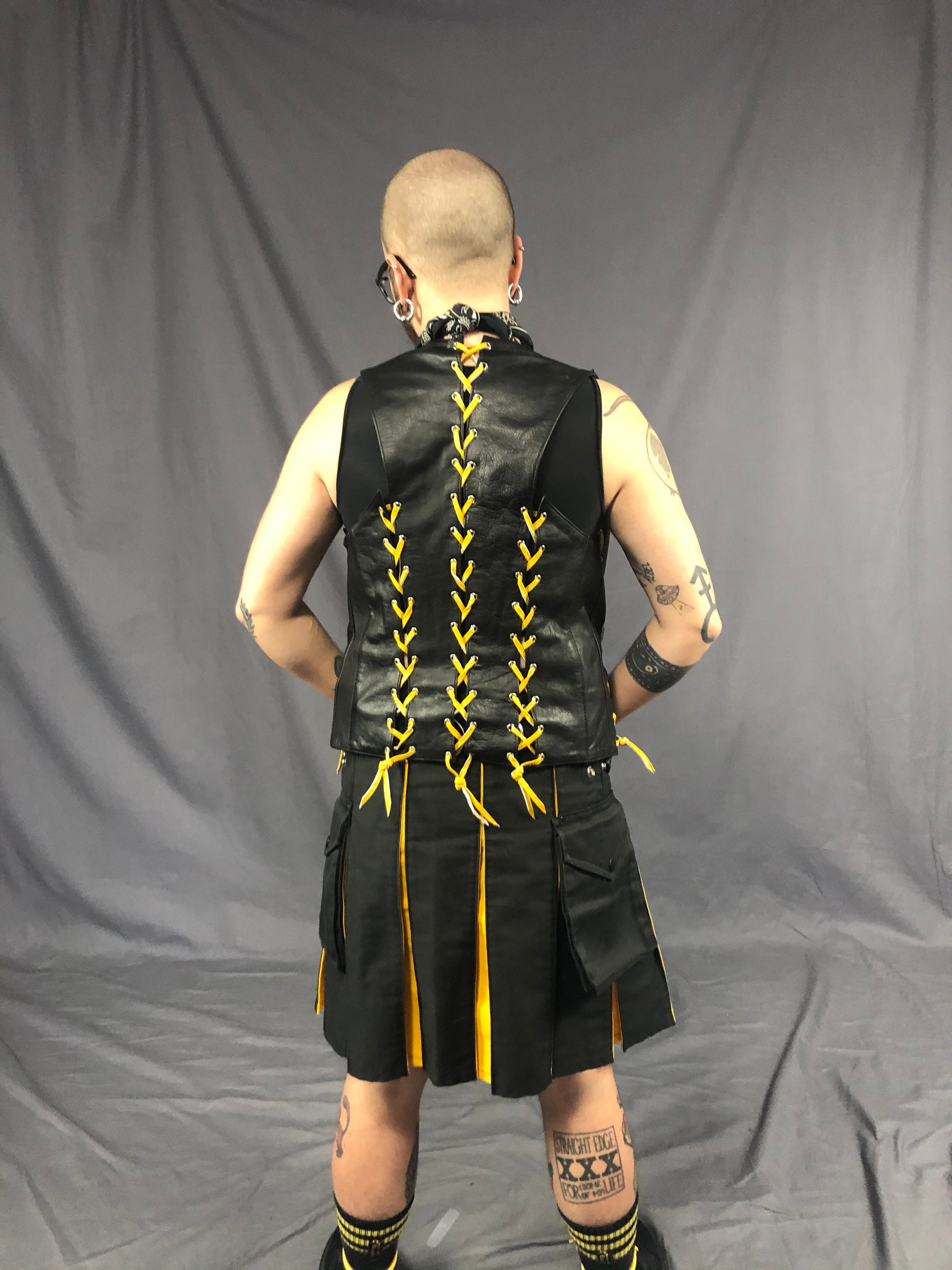 Back view of front & back lace cowhide bar vest with yellow laces, matched with a black kilt with yellow panels.