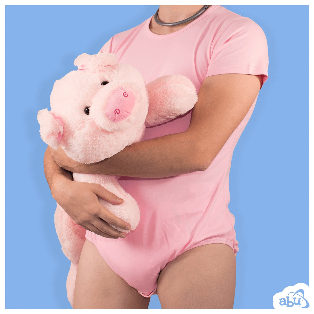Front view of model wearing baby pink diapersuit with disposable diaper worn underneath and holding a stuffed pig
