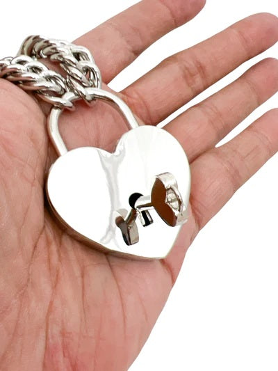 A hand holding the silver Jumbo Heart Lock that is attached to a chain. The key is in the key hole.