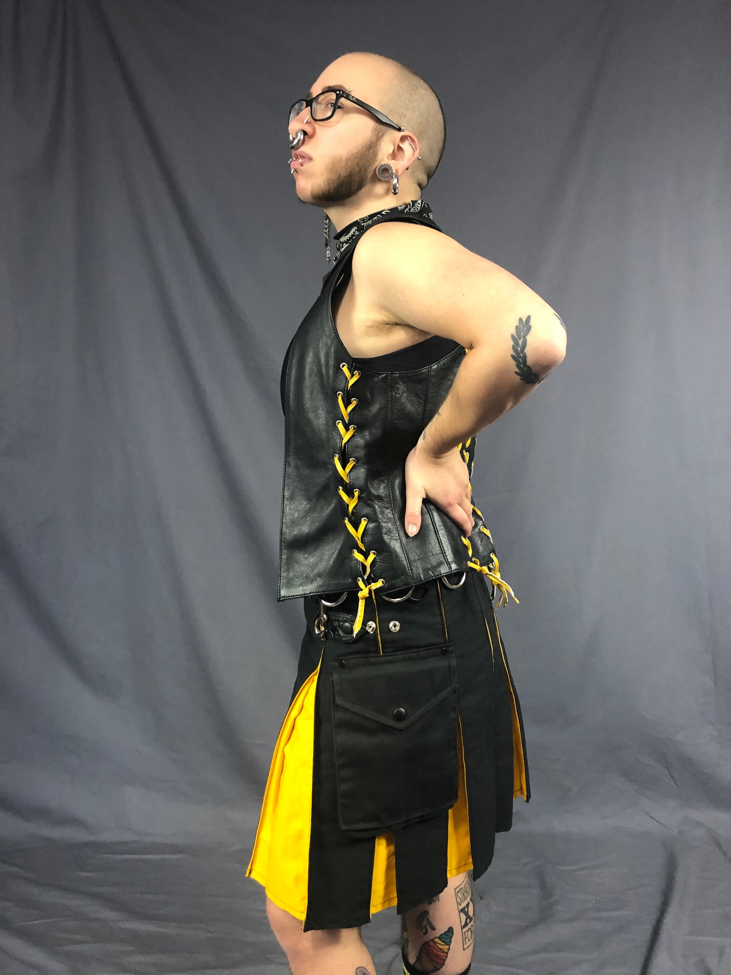 Left side view of front & back lace cowhide bar vest with yellow laces, matched with a black kilt with yellow panels.