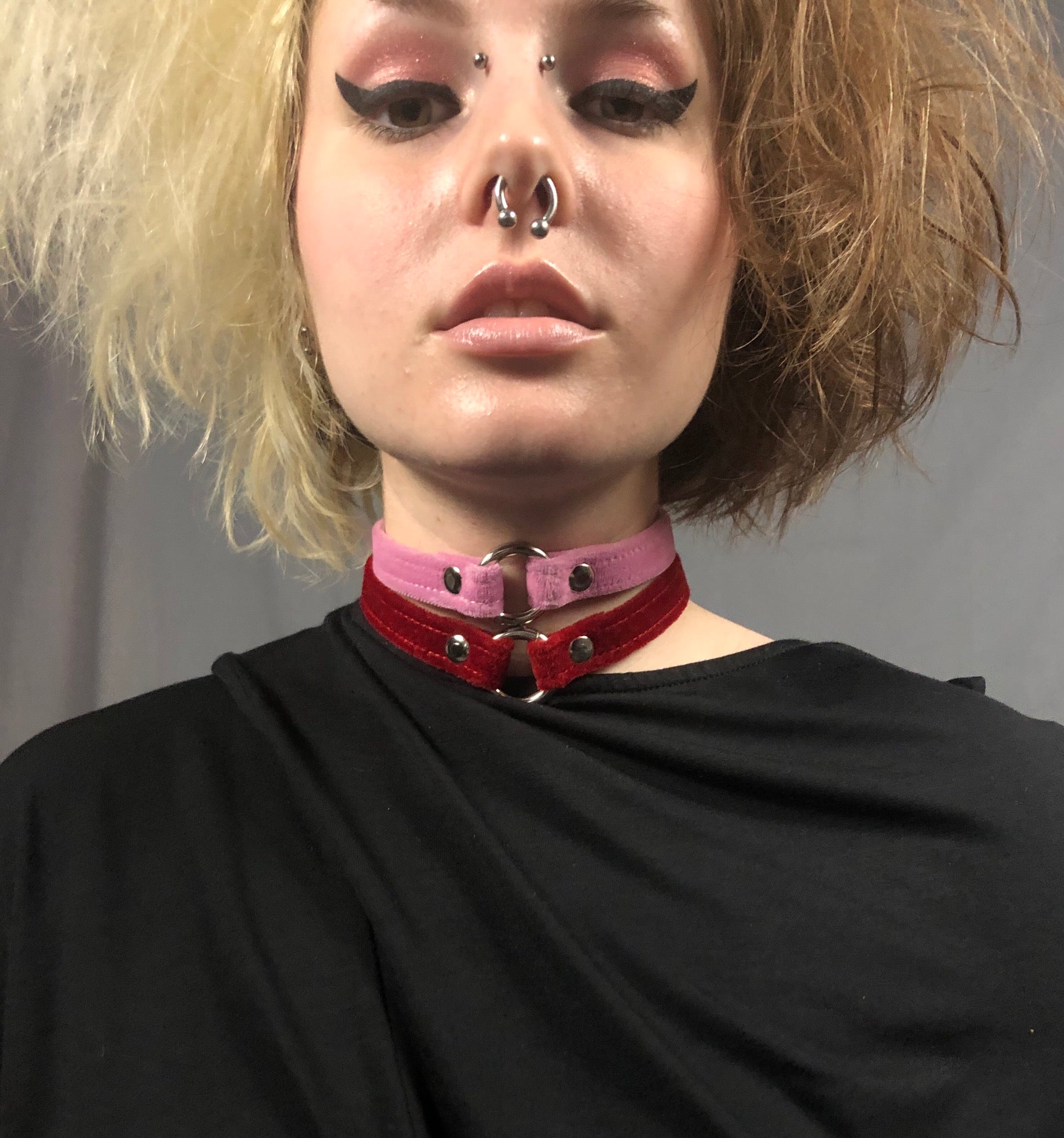 A model with facial piercings, wears two Velvet Chokers, pink and red.