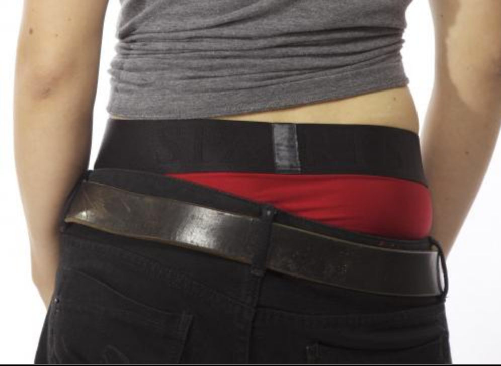 A model wearing black jeans displaying the waistband and some of the back of the red Tomboi Brief Harness.