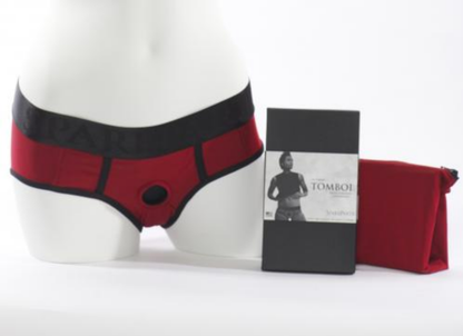 The red Tomboi Brief Harness on a mannequin displayed next to its packaging.